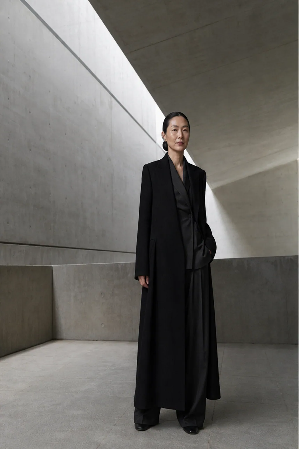 成年女性建筑师身穿黑色长外套站在混凝土展厅的写实照片
